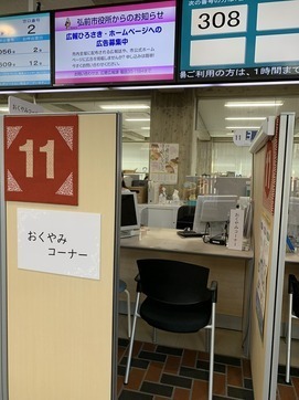 おくやみコーナーは市民課11番窓口にあり、プライバシーの確保のためボックス型の仕切りを置いて中には２名ほどが座れるようになっています。窓口の机の上にはコロナ対策のため透明アクリル板を置いています。